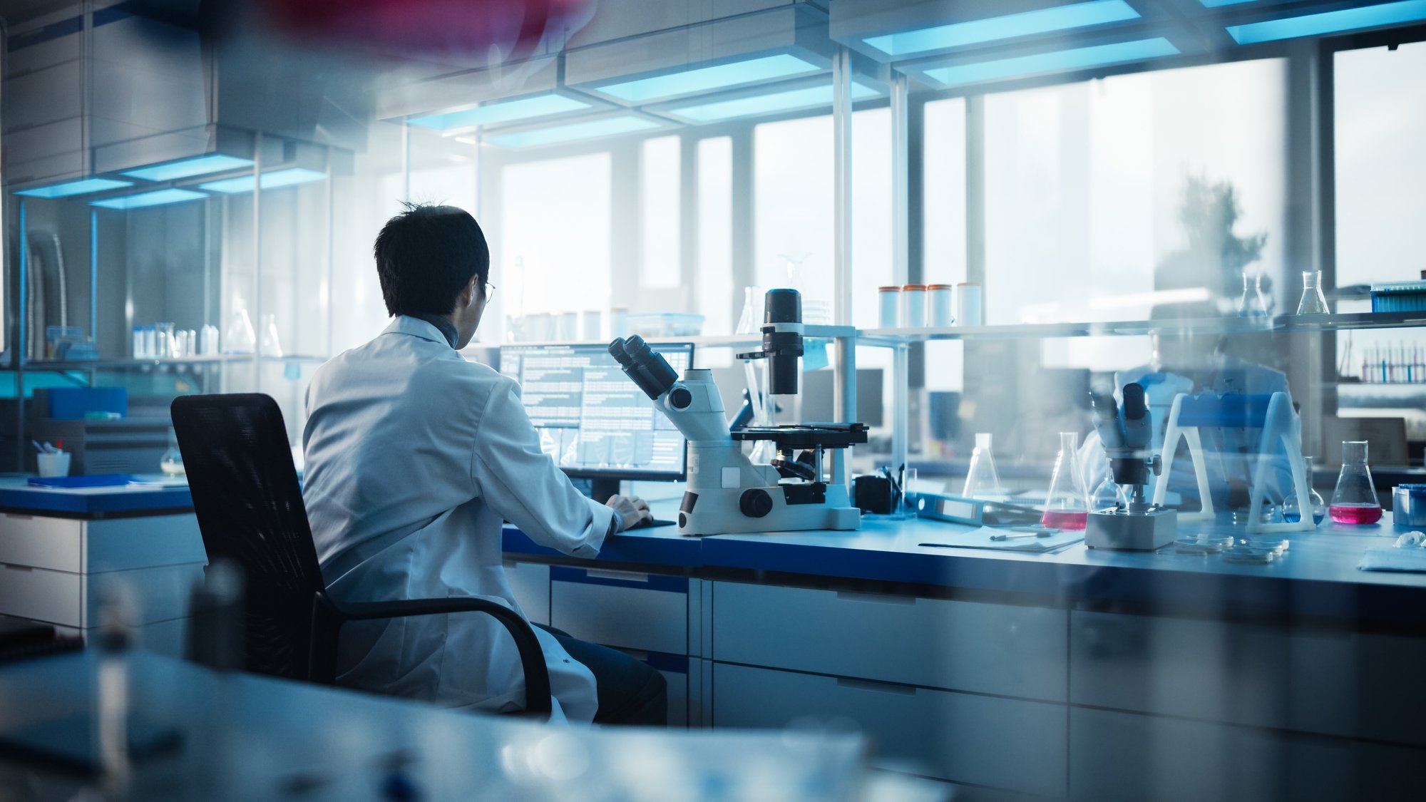 medical-development-laboratory-back-view-japanese-male-scientist-using-touch-screen-digital-tablet-computer-doing-data-analysis-research-biotechnology-specialists-advanced-scientific-lab